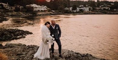 Groom and Bride with white monochrome bouquet in hand, standing on rocks alongside the ocean